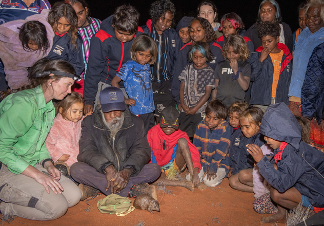AWC Field Ecologist Aliesha Dodson and Newhaven Ranger Benedict Mosquito with students from Nyirripi School release a Golden Bandicoot inside the predator-free area. 